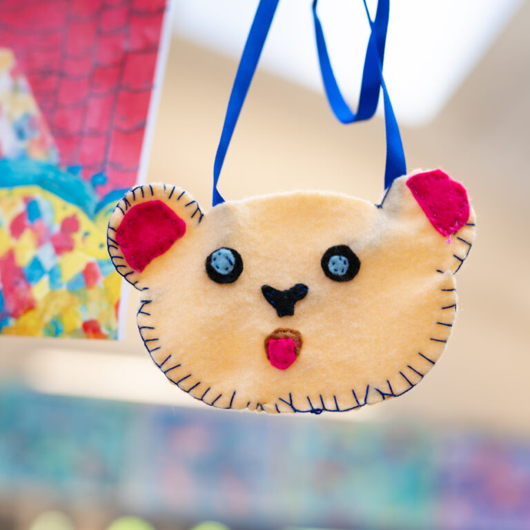 Handmade felt bear ornament hanging by a blue ribbon, pink ears and stitched edges.
